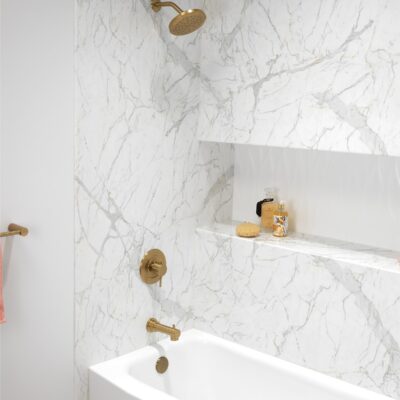 White marble shower with recessed shelf and gold faucets